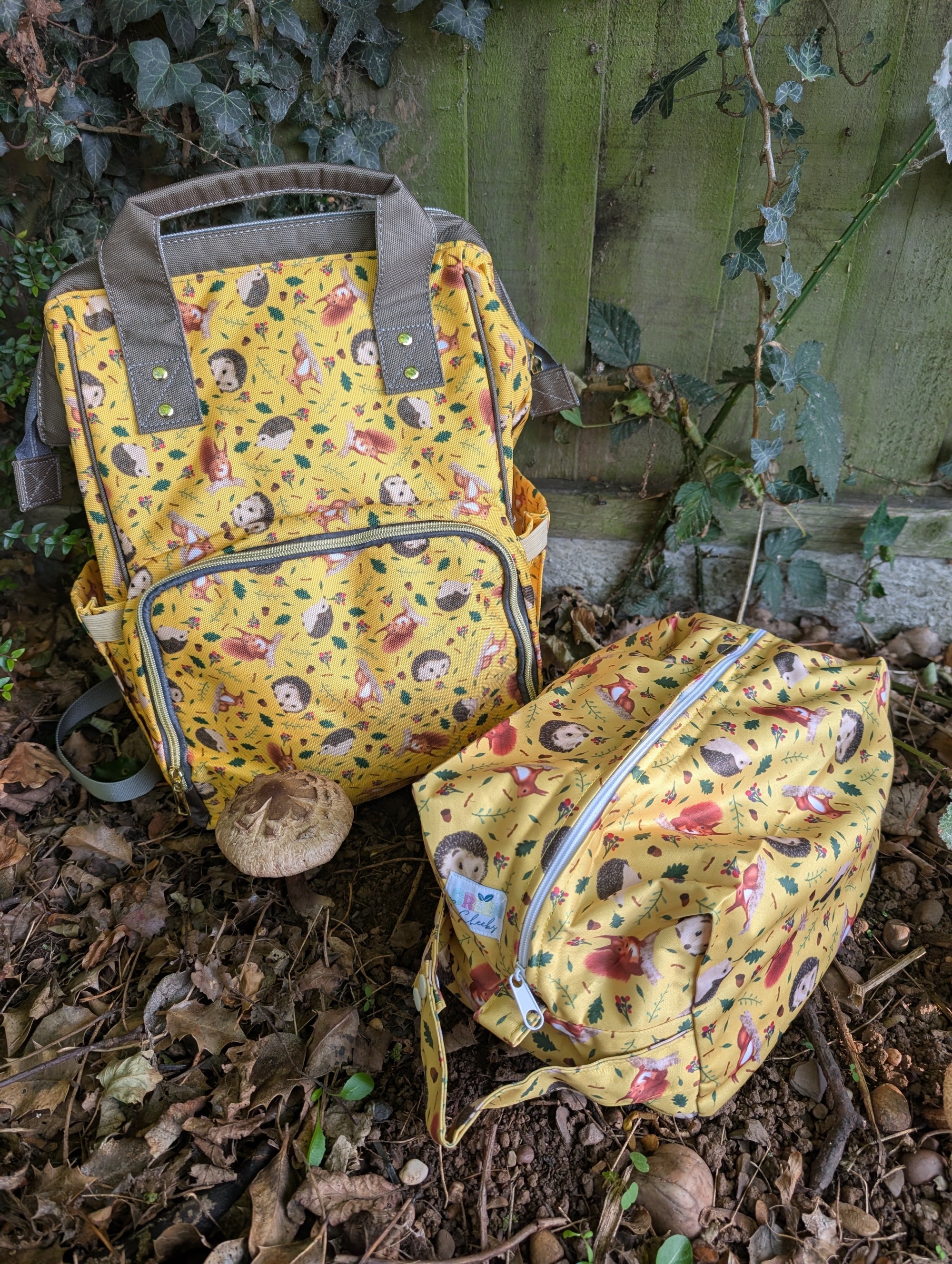 Yellow patterned backpack and pouch on a leafy ground with a wooden fence in the background