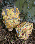Yellow patterned backpack and pouch on a leafy ground with a wooden fence in the background