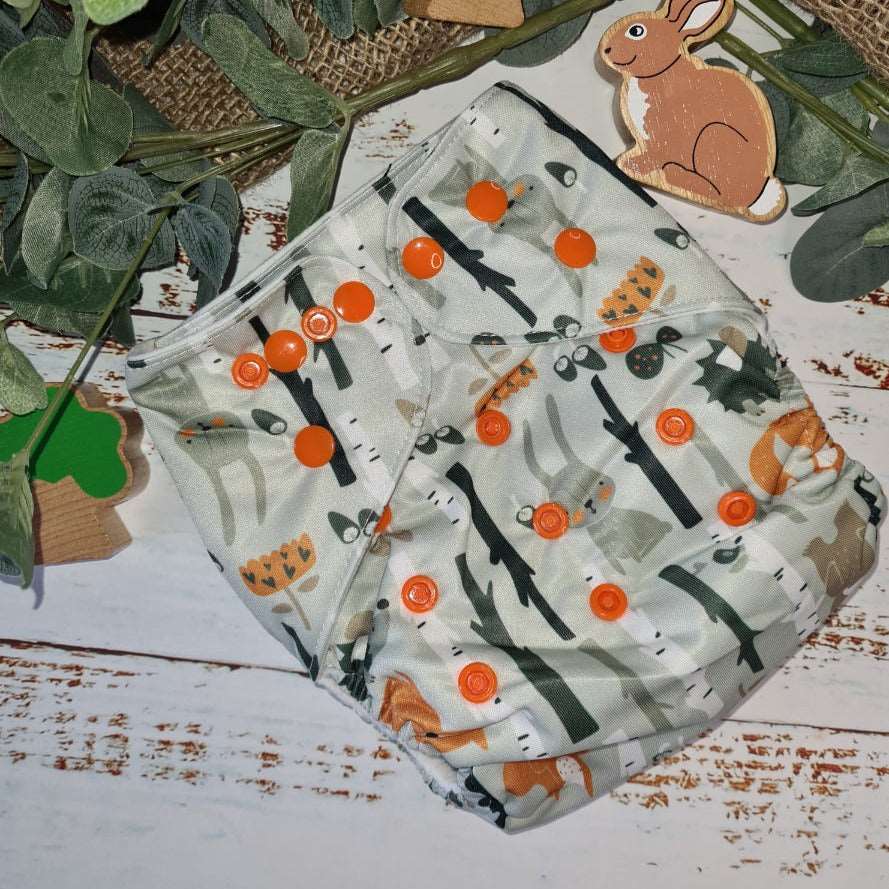 A close-up image of cloth pocket nappies in a woodland animals print, highlighting their adjustable snaps and sustainable materials.