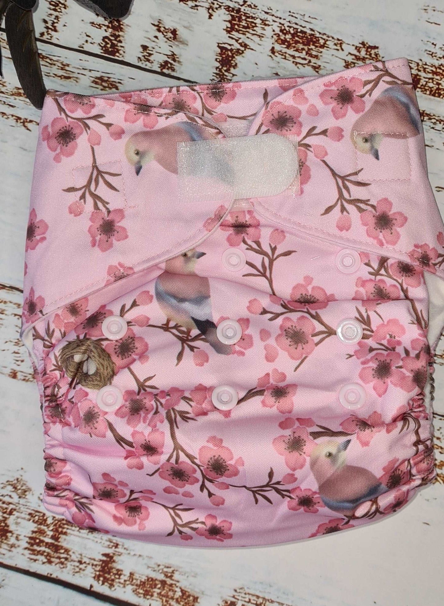 A photograph of cloth diaper pocket nappies and hemp boosters, illustrating their eco-friendly and adjustable design. features pink blossom and jay birds. 