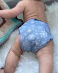 Green Cheeks Winter Cloth Nappy in a icey print is worn by a cute baby on fluffy white blanket