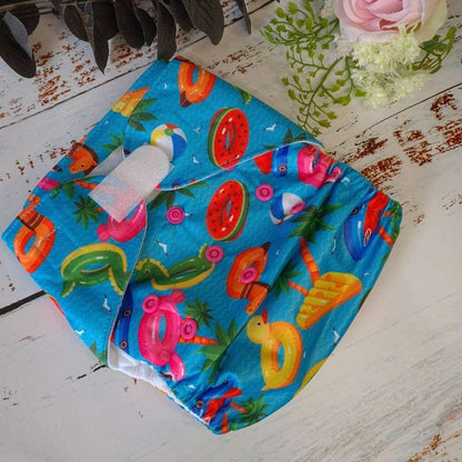 Cloth pocket nappies with hemp boosters in various vibrant colors, providing a sustainable way to keep babies comfortable and dry in blue with a pool party scene. 