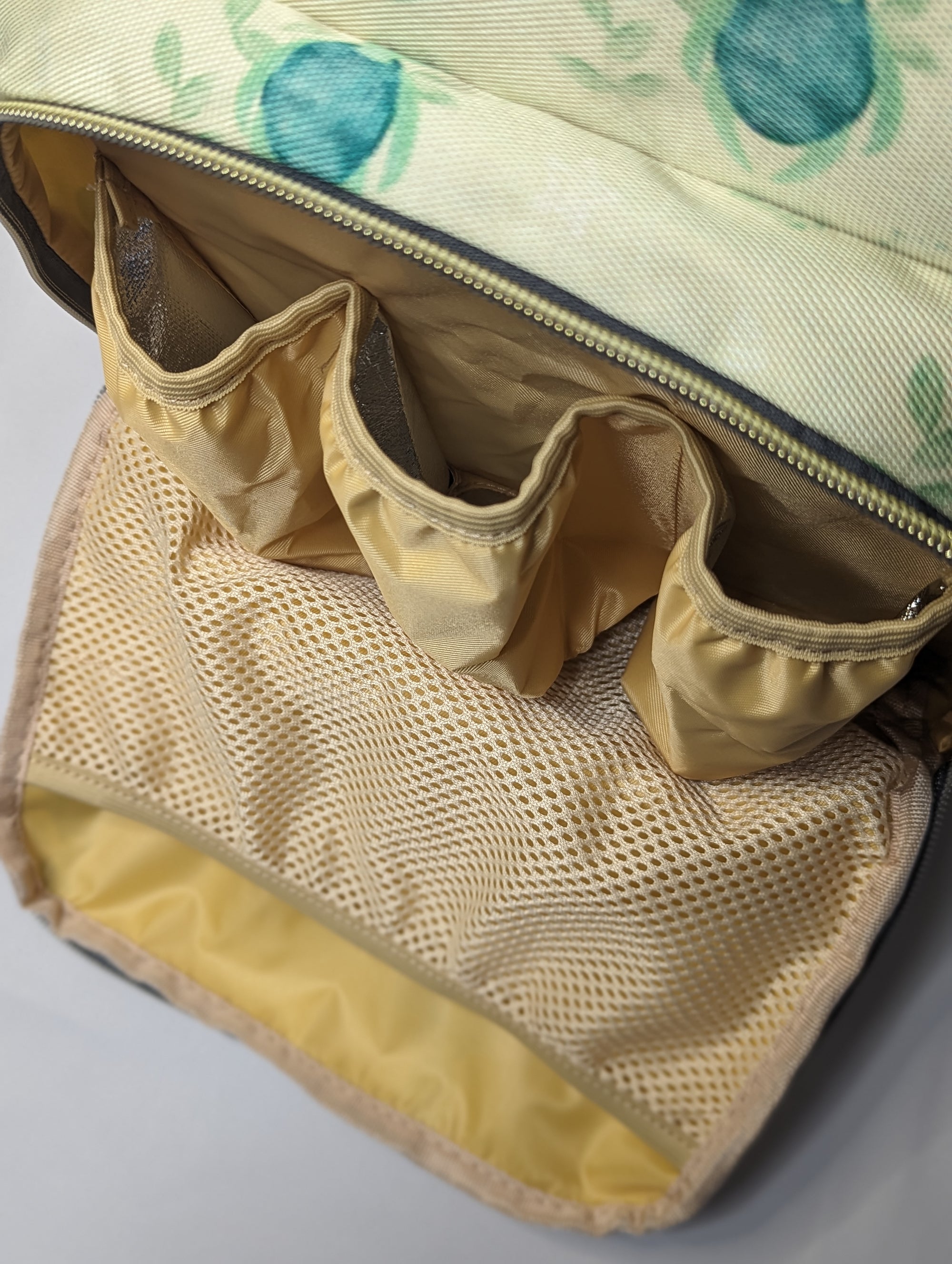 Floral-patterned bag with beige interior and mesh pocket on a light gray background