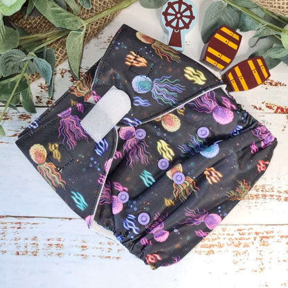 An overhead view of cloth pocket nappies and hemp boosters, an excellent choice for eco-conscious parents in a black and purple under water print. 