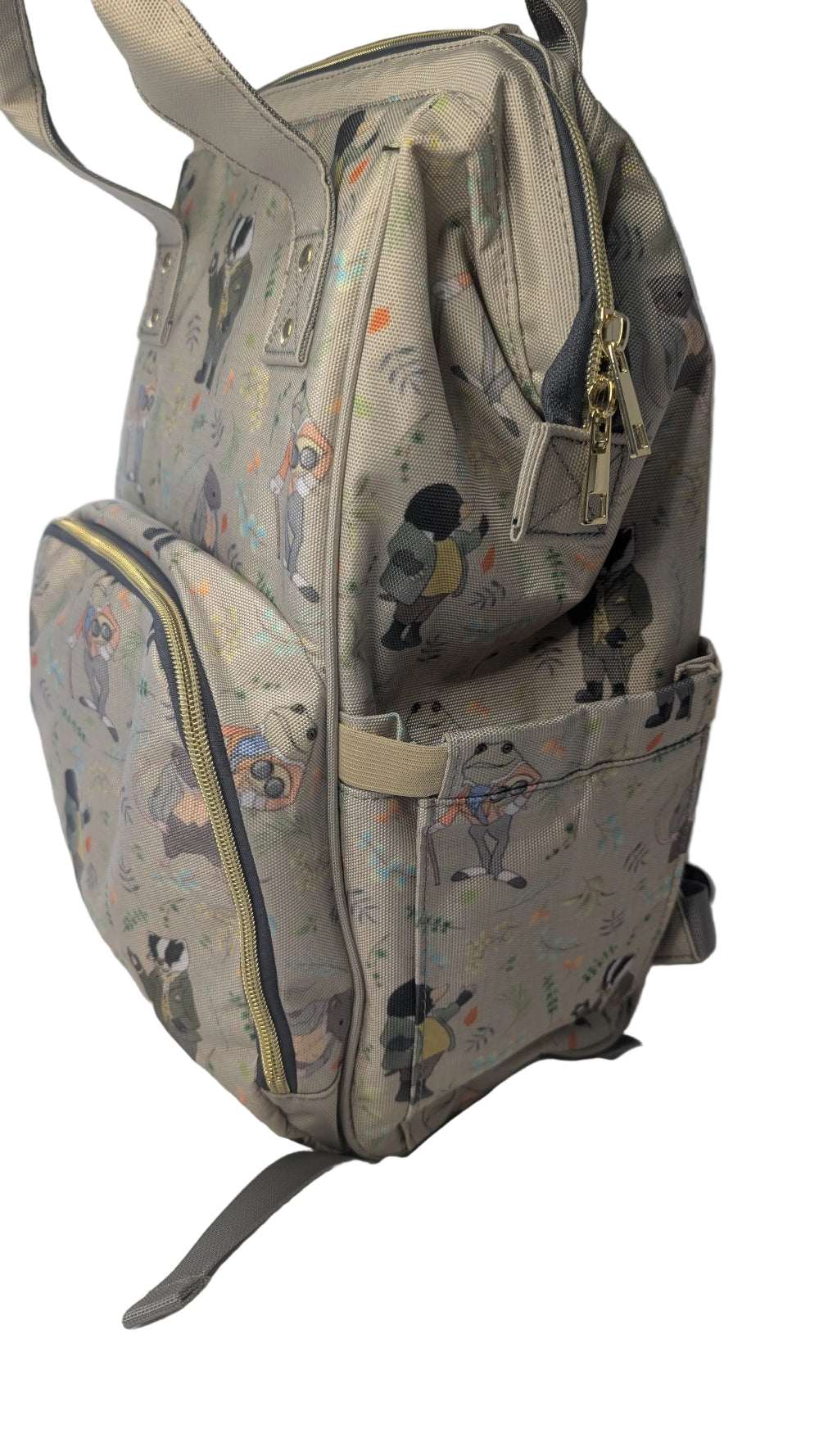 A light beige backpack with a whimsical cartoon character print, featuring multiple zippered compartments and a front pocket, resting on a white fabric surface.