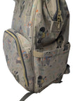 A light beige backpack with a whimsical cartoon character print, featuring multiple zippered compartments and a front pocket, resting on a white fabric surface.
